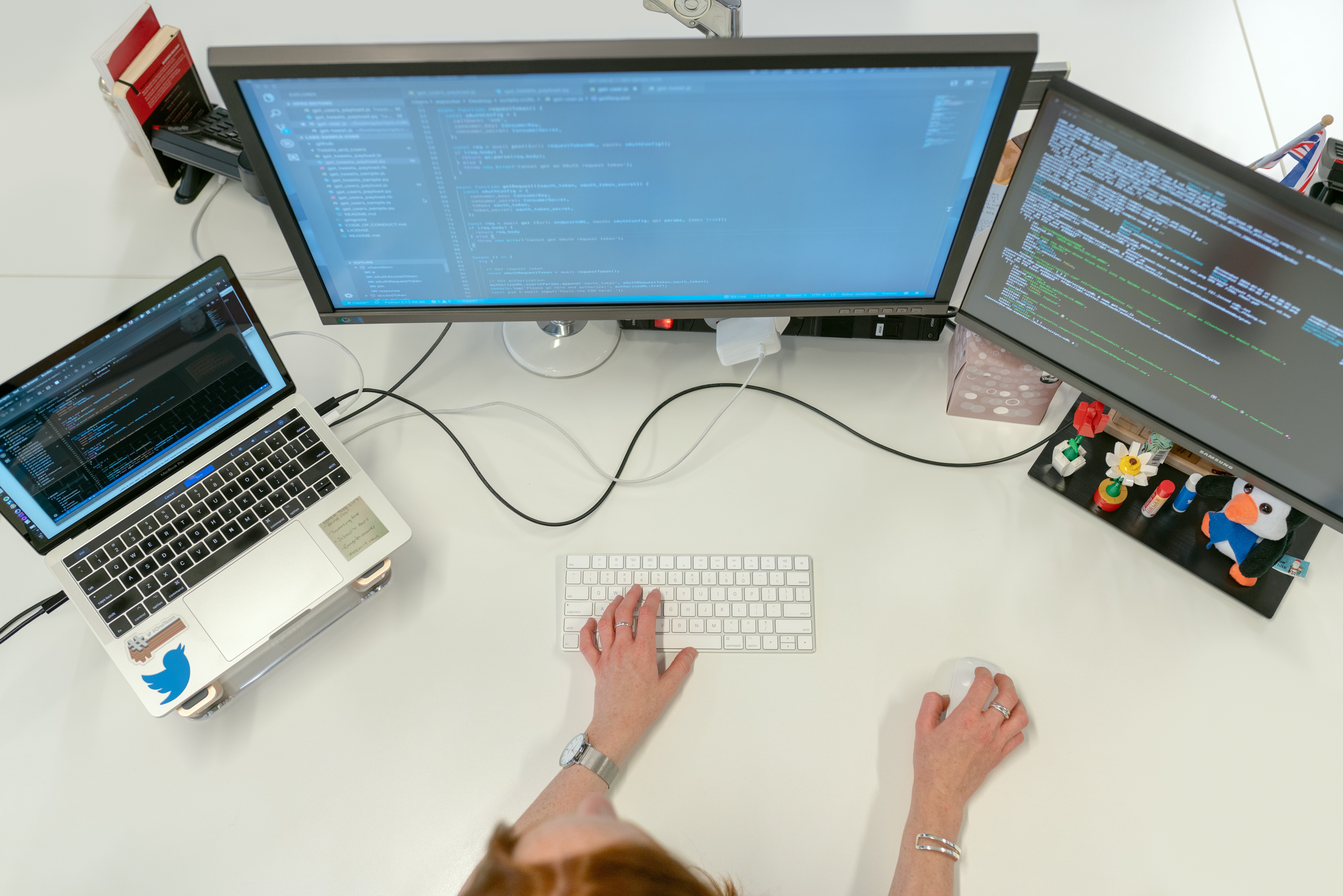 An overhead view of a software engineer's desk featuring two monitors displaying code and a laptop.
