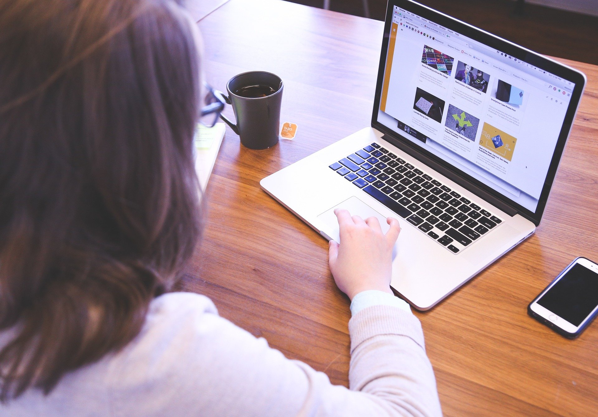 Une femme est assise devant un ordinateur qui affiche une page Web contenant six images. Elle a une tasse de café à sa gauche et un téléphone à sa droite.